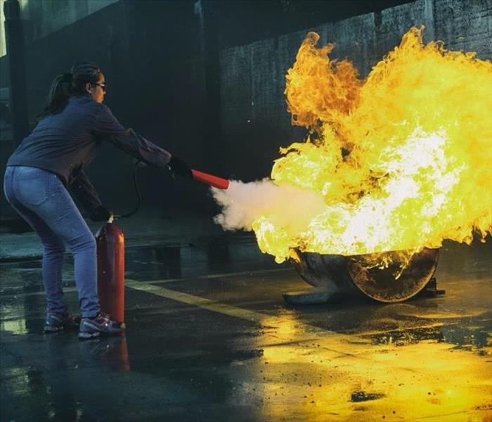 woman using fire extinguisher putting out a fire on a cement sidewalk